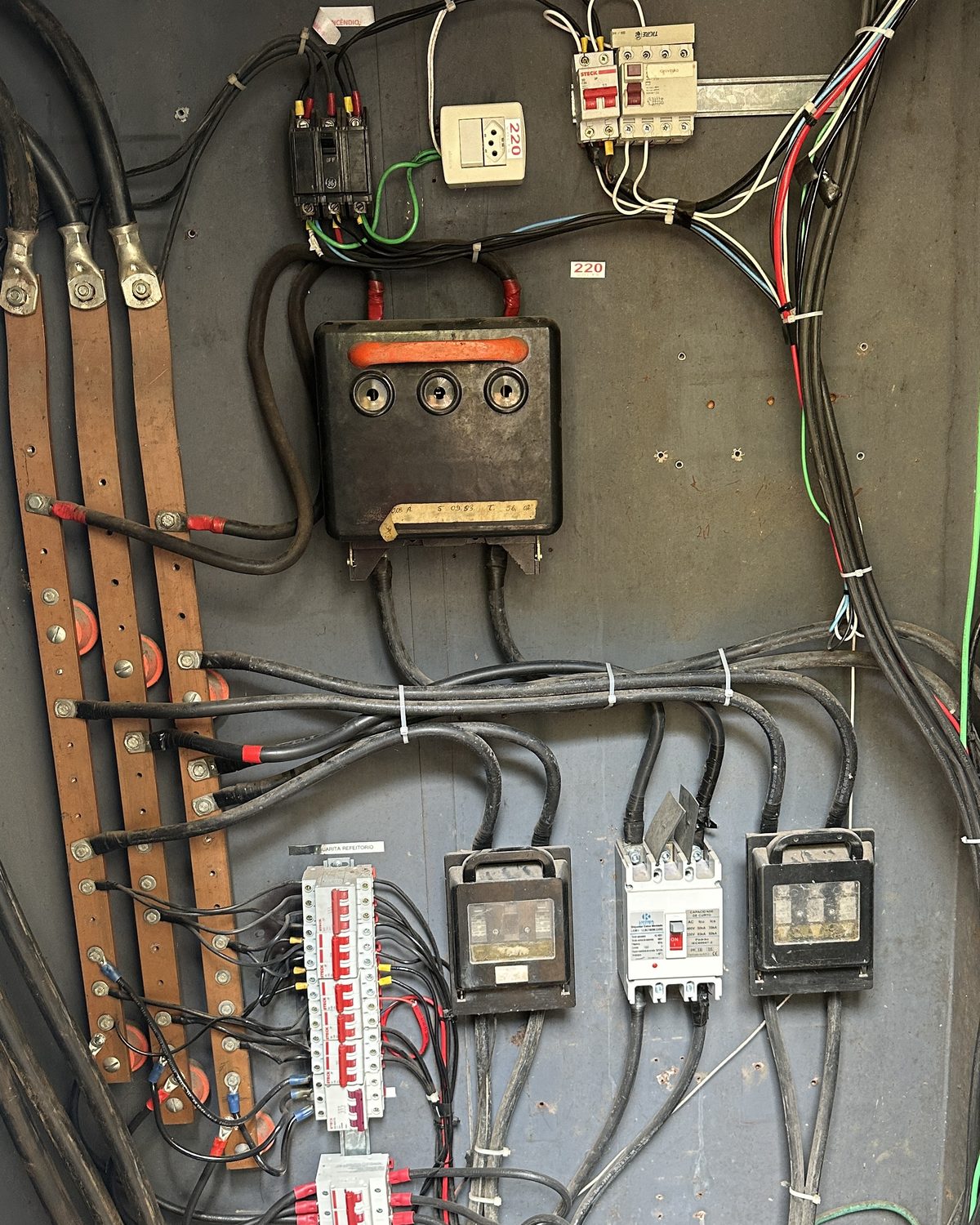 Quadro elétrico antigo do colégio, com fusíveis e fiação desorganizada